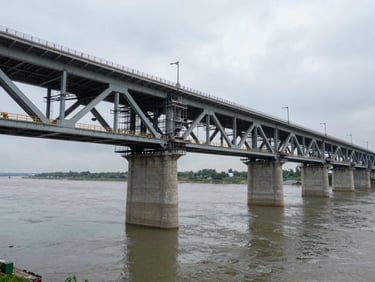 Elevated wide shot of a completed bridge structure at overcast daylight, concrete piers and deck visible, river below, no workers, engineering scale evident