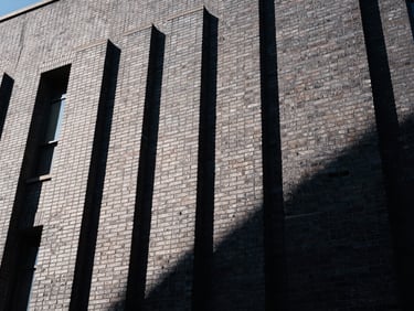 Low-angle architectural shot of a massive commercial brick facade, sharp afternoon sunlight casting crisp geometric shadows, deep charcoal masonry joints, 35mm photography.