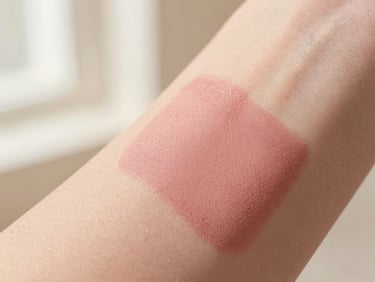 Close-up of a soft liquid blush swatch on warm skin, showing realistic skin texture, soft-focus background, warm cream tones