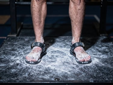 athletic photography, close-up of a weightlifter's feet firmly planted on a textured platform, chalk visible, focused overhead spotlighting.