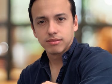 Professional portrait of a young man with dark hair wearing a navy blue button-down shirt.