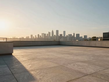 Cinematic wide shot of a minimalist penthouse terrace at golden hour, warm light pooling on pale stone pavers, the city skyline visible as a soft blur on the horizon, no occupants, deep shadow in the foreground corners