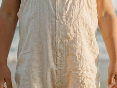 Tactile close-up of durable flat-felled stitching on a child's linen romper, warm golden-hour light, soft focus, 35mm film