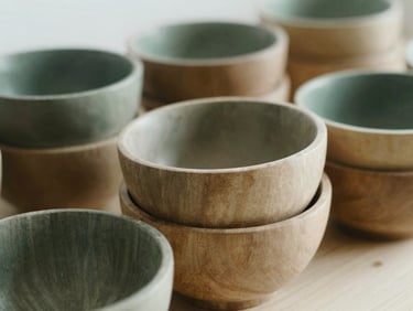 Close-up of a perfectly stacked set of handcrafted wooden bowls on a light surface, soft natural side-light, shallow depth of field, muted forest green and beige tones.