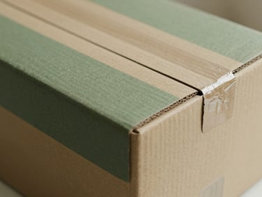 Clean, minimalist image of a custom branded cardboard box being carefully sealed, focusing on the texture of the box and the precision of the sealing tape, warm side-light
