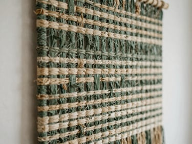 Textural close-up of an intricate woven wall hanging in a minimalist interior, soft diffused natural daylight, muted forest green and beige tones, shallow depth of field.