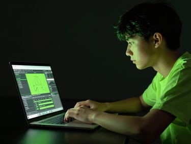 Focused shot of a student in a dark classroom setting, neon green light reflecting on a laptop screen, learning content creation