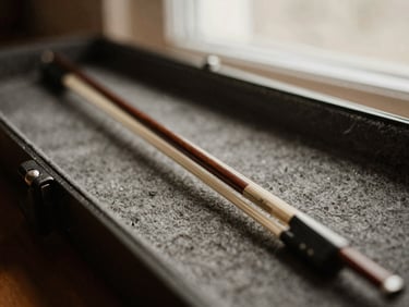 Close-up of a weathered cello bow resting on an open case, with soft natural light filtering in, warm editorial photography, charcoal tones, intimate shallow depth of field.
