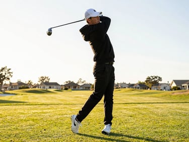 Low-angle candid shot of a stylish golfer in a black hoodie mid-swing on a pristine course, bright golden hour sunlight, high contrast, streetwear aesthetic.