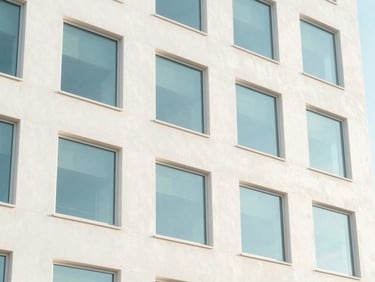 Bright, airy architectural detail of a modern Florida office building with soft morning shadows on clean white concrete, pastel sky blue reflections in the windows