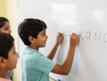 Happy Indian boy tracing letters on a whiteboard with a teacher's gentle guidance, bright classroom, candid.