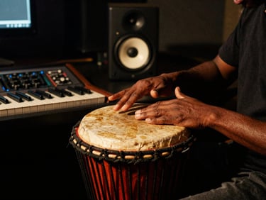 Behind the scenes close-up of hands adjusting a traditional Ugandan drum next to modern studio monitors, warm chiaroscuro lighting.