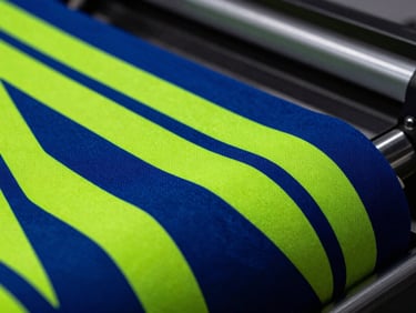 Macro close-up of a vibrant sublimated fabric roll with sharp geometric neon patterns, industrial heat press environment, dramatic side lighting, 35mm lens