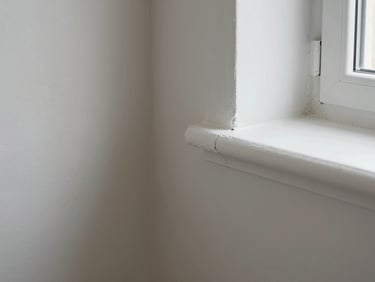 Close-up of a freshly painted interior wall corner meeting white trim, soft natural light from a nearby window, crisp edge with no brush marks visible