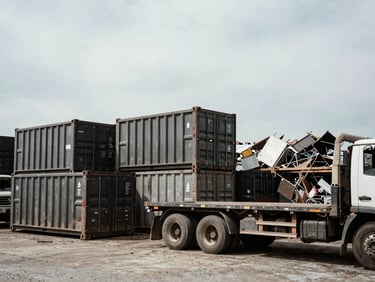 Wide shot of various heavy-duty industrial roll-off containers and flatbed trucks in a scrap yard, overcast Pennsylvania sky, high contrast, gritty industrial photography