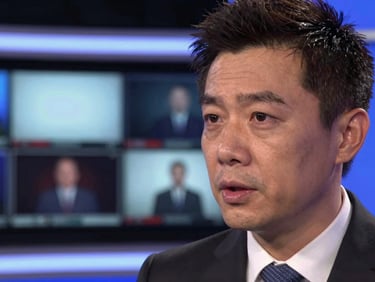Close-up of a news anchor mid-sentence at a broadcast desk, live monitor glowing behind, high-contrast studio lighting, serious delivery, documentary framing