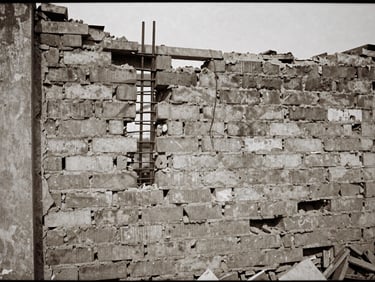 Gritty documentary film photograph of a demolished brick wall with steel rebar exposed, harsh natural daylight, muted earth tones, 35mm grain