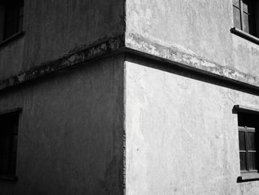 High-contrast monochrome medium-format film photograph of a weathered concrete building corner in harsh midday sun, deep shadows, gritty 35mm grain