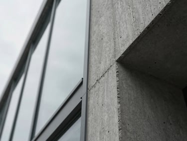Extreme close-up architectural detail of raw concrete meeting structural glass, low-angle overcast diffuse daylight, focusing on material intersection