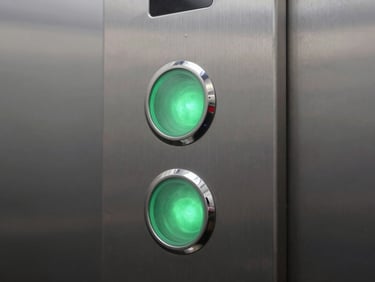 Macro shot of a high-quality brushed steel elevator button panel with crisp green LED illumination, clean architectural lines, cool lighting