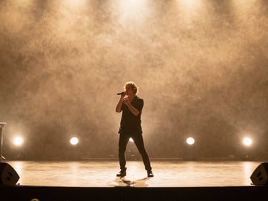 Cinematic wide shot of an artist performing on a warm, sunlit stage, soft stage flares, golden-hour backlighting, 35mm film look.