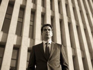 Monochromatic portrait of a distinguished man in a suit, sharp architectural background, low-sun golden hour light, editorial style