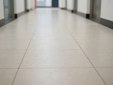 Close-up of a freshly mopped hard floor in an empty commercial corridor, natural daylight, clinical sharpness showing grain of clean tiles