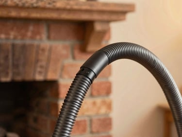 Close-up of a modern HEPA dust-containment vacuum hose near a clean brick hearth, warm golden-hour light, shallow depth of field