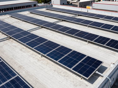 Wide-angle architectural shot of a large industrial rooftop in Monterrey with high-efficiency solar arrays and neatly routed conduits, harsh bright Mexican sunlight, high-contrast blue and amber tones, 35mm