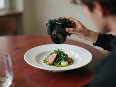 Candid behind-the-scenes agency moment of a photographer adjusting a camera lens over a beautifully plated dish, warm indoor glow, 35mm film