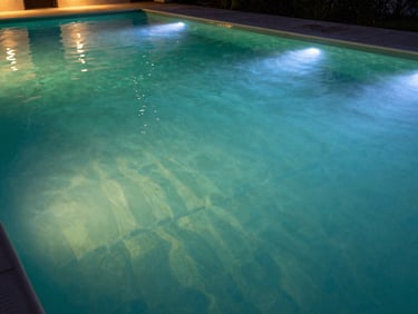 Wide shot of a pool transitioning from green-tinted water to clear blue at the far end, dawn light, architectural pool surround, no people