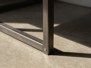 Architectural close-up of a minimalist metal furniture joint in hard direct sunlight, casting a sharp shadow onto a warm concrete floor, medium format