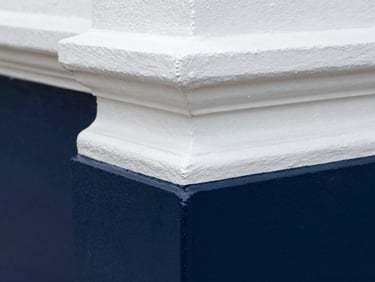 Macro close-up of a razor-sharp navy blue paint line against stark white historic trim.