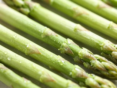 Macro detail of crisp green asparagus spears flecked with water droplets, bright morning light, shallow depth of field