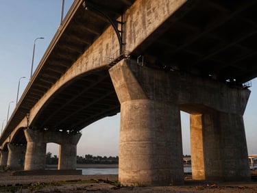 Low-angle wide shot of a massive concrete and steel bridge structure, dramatic long shadows, golden hour, 35mm.
