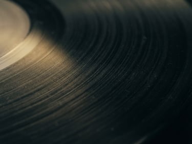 close-up of a vinyl record groove with subtle gold light leaks, atmospheric cinematic photography, low-key lighting, deep shadows, moody desaturated tones, 35mm film