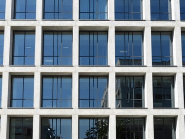 Straight-on architectural photograph of a modern multi-story office building with clean concrete pillars and glass facade, bright daylight