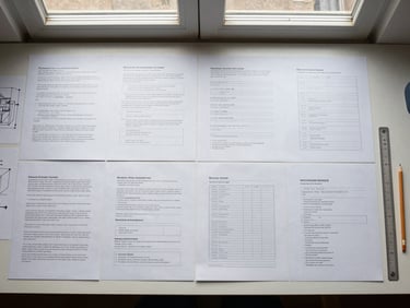 Overhead flat lay of a clean workspace with structured business model documents arranged in deliberate order on a light surface, architectural diagram sketches visible, a ruler and pencil placed at the edge, north-facing window light creating even soft shadows