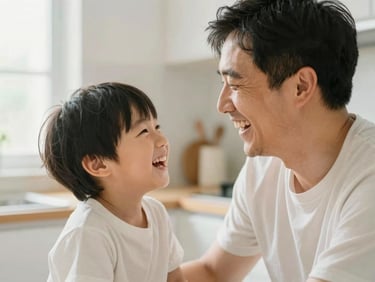 A father laughing with his young son in a sunlit kitchen, warm editorial photography, soft clean color palette, shallow depth of field