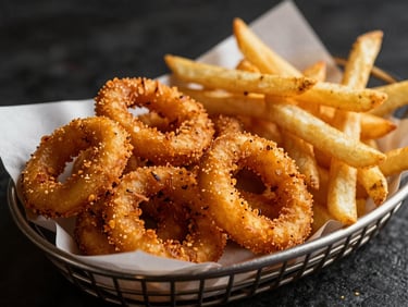 A basket of golden crispy onion rings and french fries on greaseproof paper, warm dramatic overhead lighting