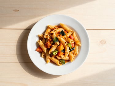 top-down flat lay of a comforting local-western main meal, e.g., pasta with colorful vegetables and sauce, on a sunlit wooden table, soft morning light, warm cream and pastel tones, shallow depth of field