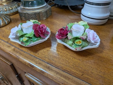 Pair of vintage porcelain floral candle holders with pink and red roses on a wooden table.