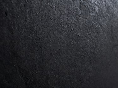 Extreme tight crop of blackened steel surface, matte oxidised finish, directional studio tungsten light revealing micro-texture, 16:9 horizontal, no context objects