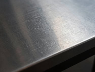 Extreme tight crop of hand-lacquered metal surface, deep gloss with visible hand-application depth, studio tungsten raking light, slight reflection visible in surface, 16:9 horizontal, no context objects