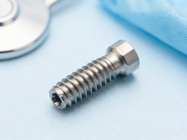 Macro shot of a high-tech titanium dental implant screw on a clean sterile light blue background, bright dental clinic lighting