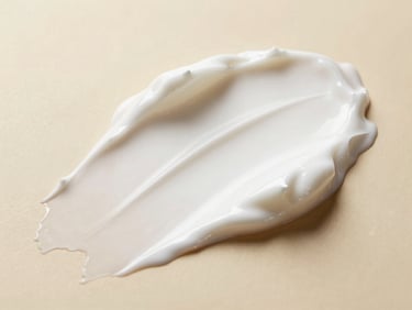 Macro shot of white cosmetic cream being smoothly spread, showing rich luxury texture, under bright clinical lighting with warm gold undertones.