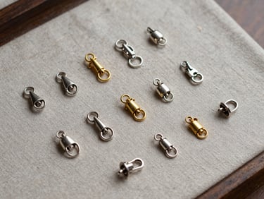 Overhead view of small silver and gold jewelry findings, clasps, and keepsake items arranged on a neutral linen surface, diffused bench light, fine detail visible