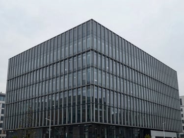 Wide shot of a modern, minimalist glass and steel commercial building in an urban setting, cool overcast daylight, desaturated tones, sharp focus.