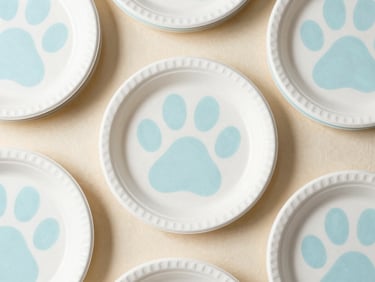 Overhead flat-lay of stacked white and pastel blue paw print party plates, clean background, soft shadows