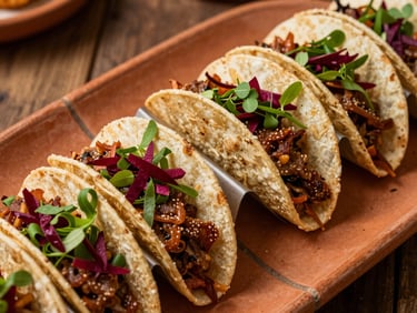 Overhead close-up of a festive holiday taco spread, deep red and green garnishes across a row of assembled tacos on terracotta serving tiles, warm tungsten light casting soft shadows